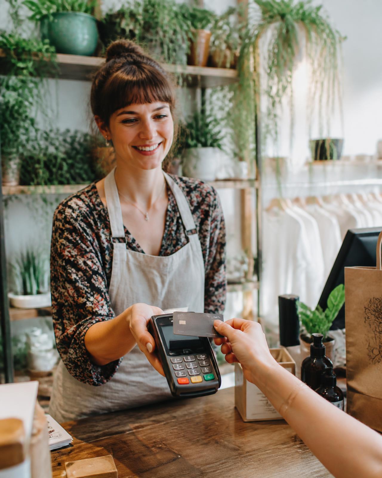 Shop owner taking a credit card payment on a terminal at a plant-filled boutique counter